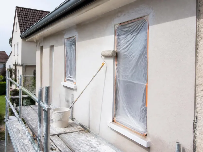 Peintre appliquant une peinture de façade au rouleau depuis un échafaudage